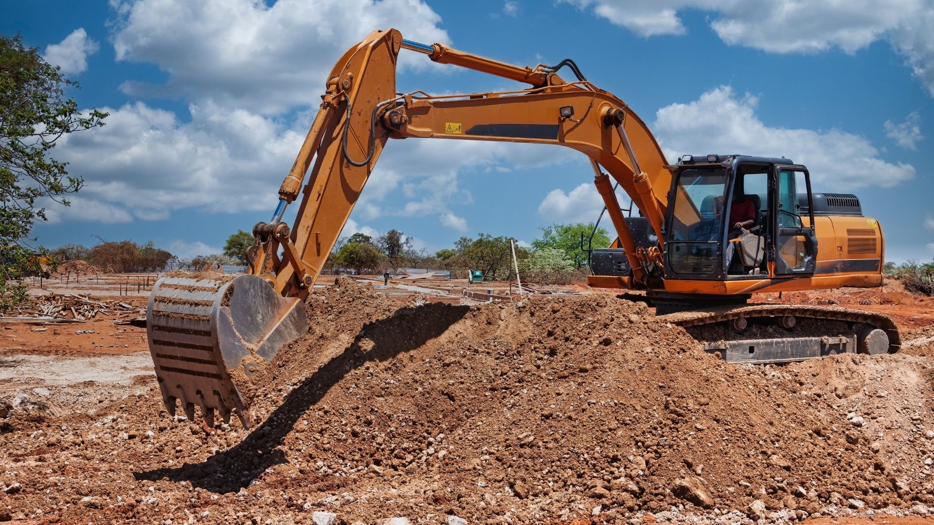 Orange excavator digging soil on construction site under blue sky with clouds
